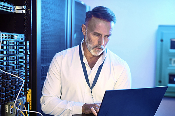 Shot of a mature man using a laptop while working in a server room Shot of a mature man using a laptop while working in a server room